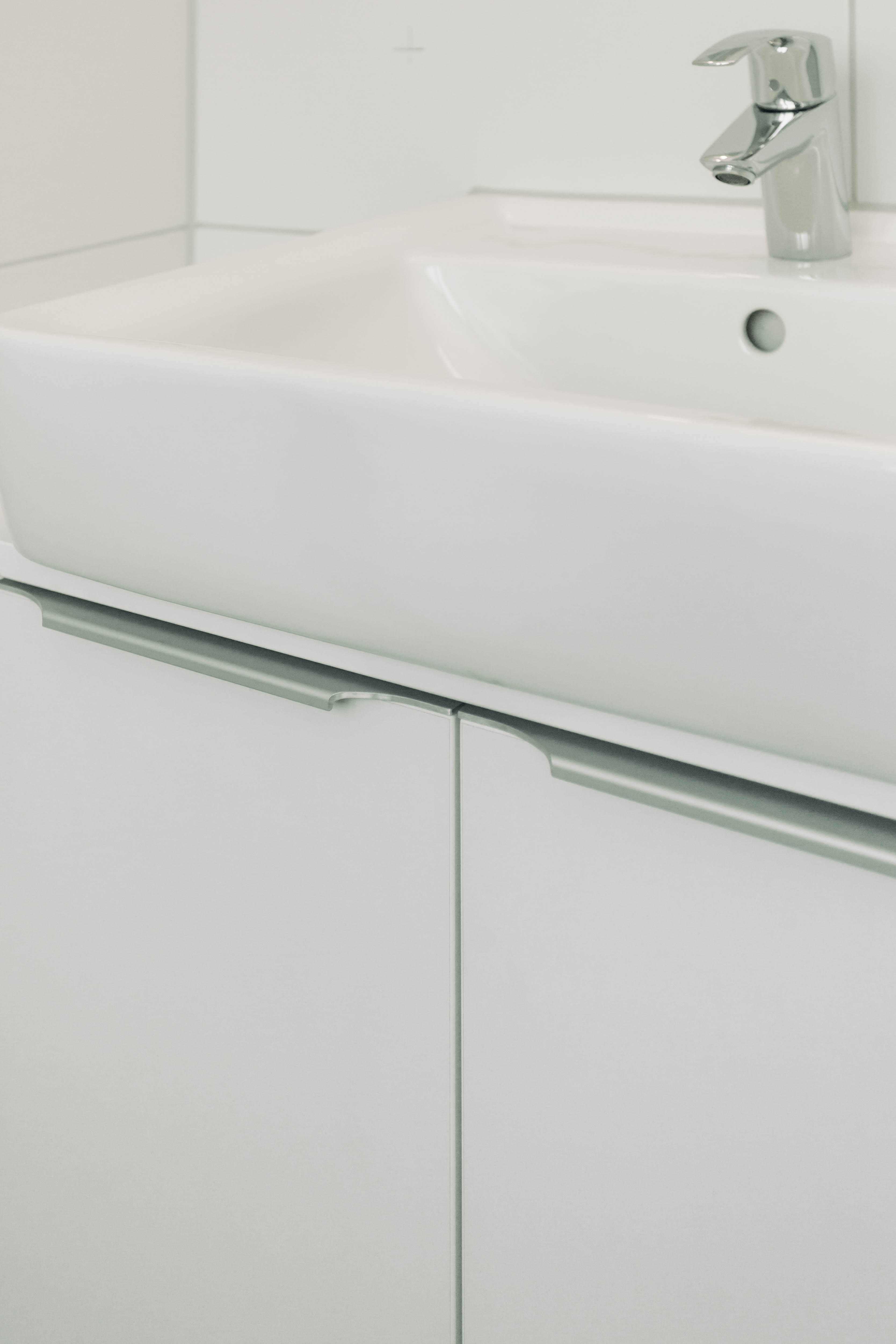 Weißer Waschbeckenunterschrank mit Aluminiumgriffen und weißem Waschbecken